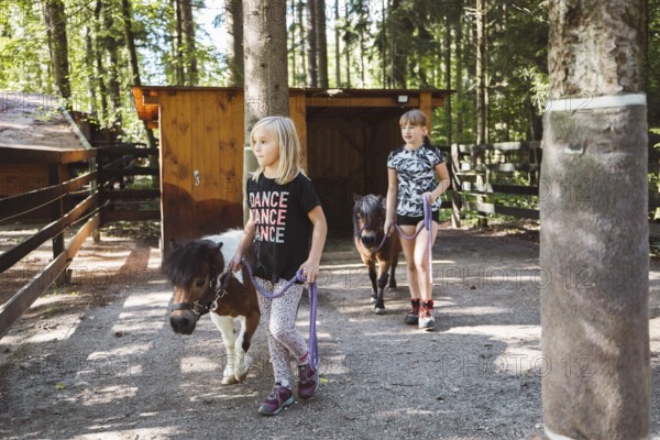 Children walking with ponies, small horses, holding them for a leash. Cute mini horses walking with
