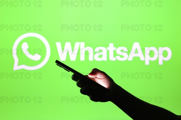 In this photo illustration the WhatsApp logo seen in the background of a silhouette hand holding a