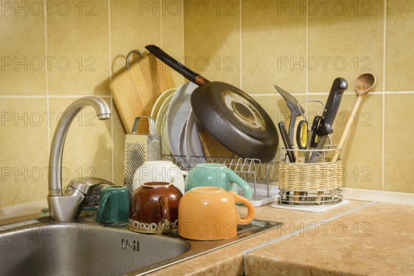 Dishes, cups, glasses, plates, forks, knives and spoons are drying close to the sink, after they