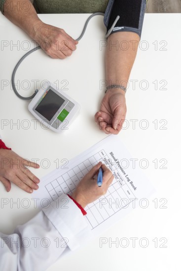 Doctor taking notes on blood pressure log book while measuring blood pressure of senior woman