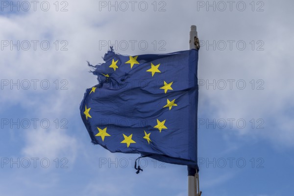 A torn EU flag blows in the wind with a few clouds in the background, seen in Pevensey Bay, East