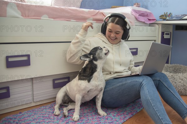 A teenager enjoys a moment of leisure in her room, working on her laptop and playing with her dog,