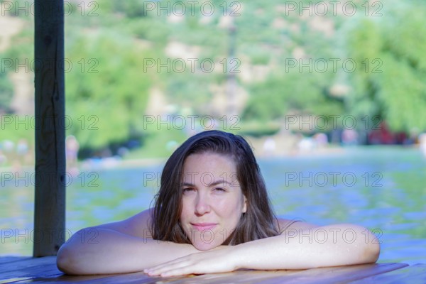 Beautiful brunette woman bathing in a lake perched on a wooden pontoon looking at the camera with a