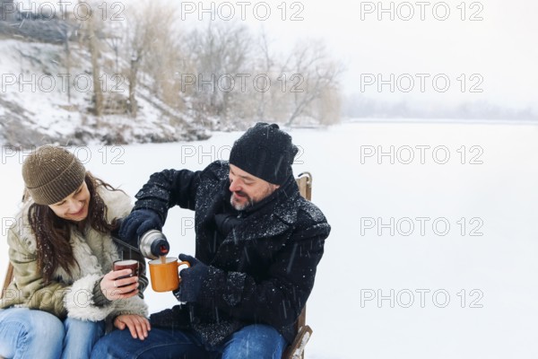 Happy lovely middle-aged couple in warm clothes drinking hot tea during romantic winter date in