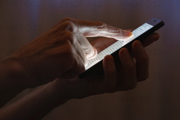 Man typing with the finger on the touch screen of a black smartphone close to the window with