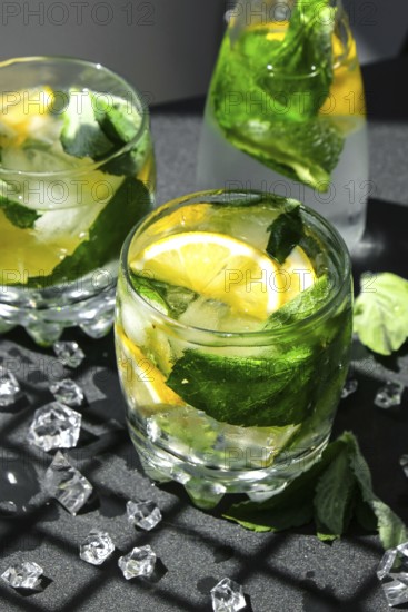 Mojito refreshing cocktail, alcohol drink. Lemonade with lemon and mint leaves on dark background.