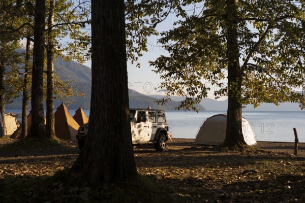 Tents and a white jeep with mountains in the background, sunrise at the lake, Shikotsu-Lakeside