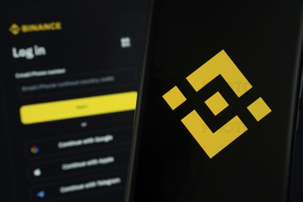 Binance logo is displayed on a smartphone screen, with the binance login page visible on a computer