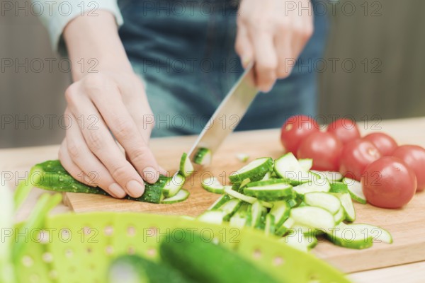 Close-up of female hands cut into fresh cut cucumbers on a wooden cutting board next to pink