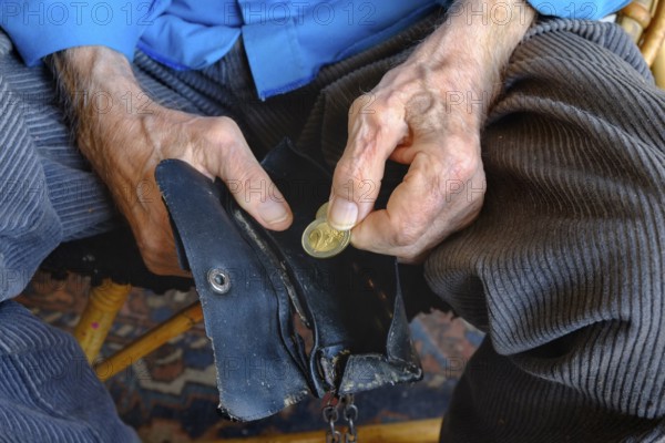An old man takes a two euro coin from his worn wallet. Close-up, landscape format. An old man takes