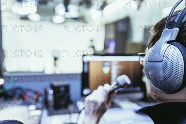 Young man is sitting in the recording studio and talks into the microphone, buttons and equipment