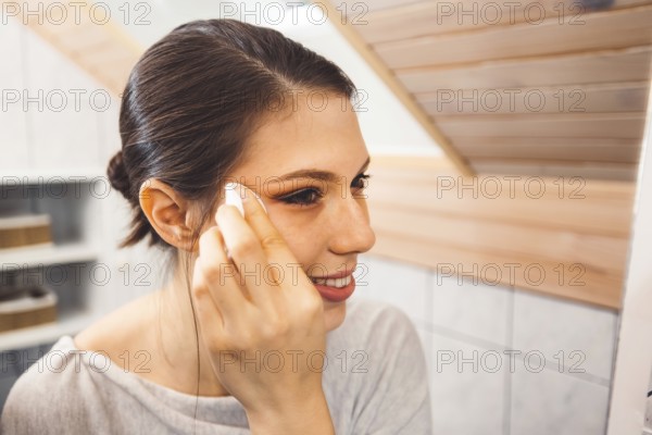 Beautiful young woman cleaning her face, removing make up with a cotton pad and micellar water.
