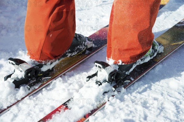 Orange alpine ski boots in a ski mount. One boot is completely fixed on skis, the second is not.