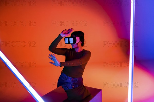 Happy female in VR headset smiling and exploring virtual reality under red neon illumination in