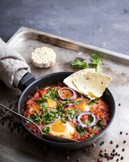 Shakshuka with pita bread in a pan. Middle eastern traditional dish. Fried eggs with tomatoes, bell