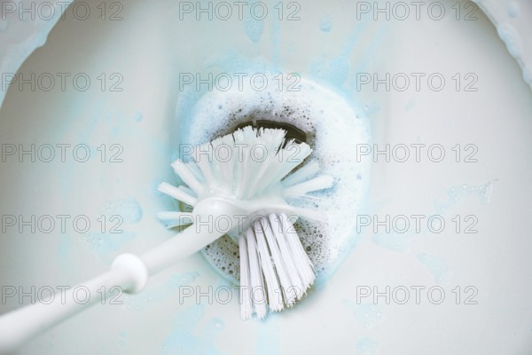 Cleaning a toilet bowl with a brush and strong chemical cleaning foam that pollutes the