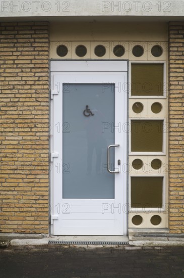 Public restroom door with accessibility sign for disabled people featuring frosted glass and white