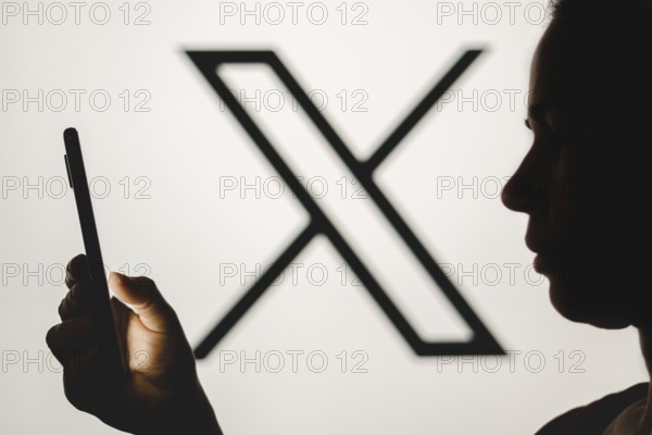 In this photo illustration, a woman's silhouette holds a smartphone with the Twitter (X) new logo
