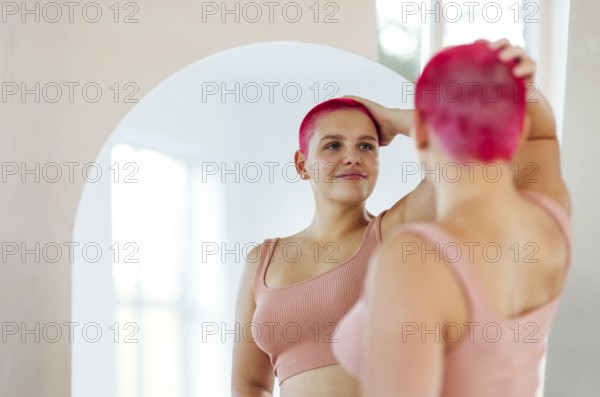 Beautiful relaxed woman in sport clothes red shot hair looking to the mirror. Concept of body