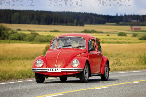 Red Volkswagen Beetle, officially Volkswagen Type 1, driving along country road on Maisemaruise
