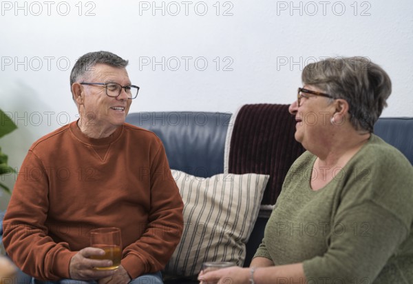 Happy retired couple enjoying a relaxing afternoon at home, sharing stories and drinks on a