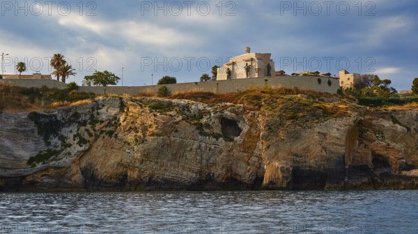 Building on a cliff under a cloudy sky next to the sea, boat trip around the island of Ortigia,