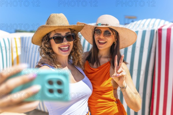 Two cheerful women wearing stylish sunglasses and trendy sun hats are capturing a joyful selfie on
