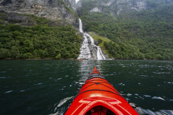 Kayak trip on the Geirangerfjord at the Freier waterfall, tip of a red kayak in the fjord,
