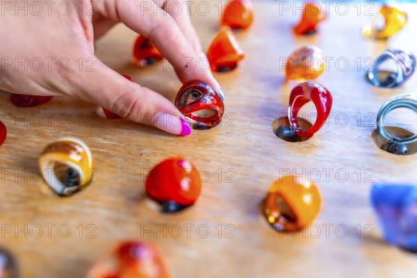 Woman's hand with pink nail polish picking up a colorful resin ring from a wooden display at a