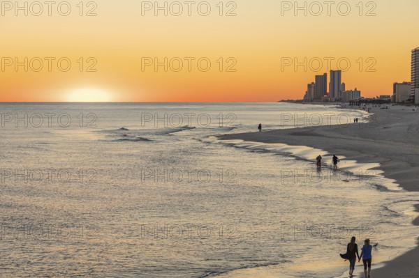 People walking and playing on the beach as the sun sets over the Gulf of Mexico at Gulf Shores,