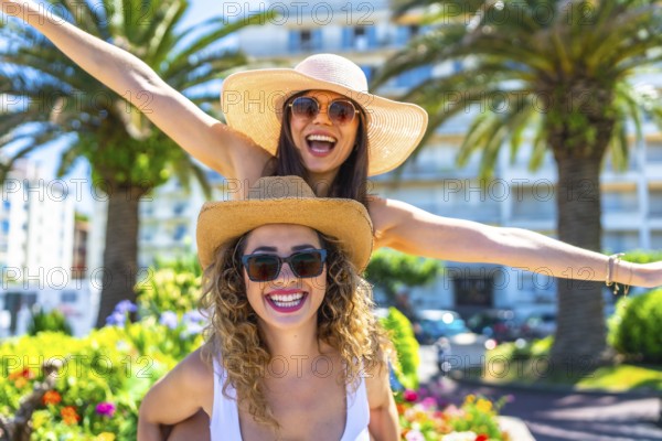 Two cheerful female friends are having fun during summer vacation, wearing sunglasses and straw