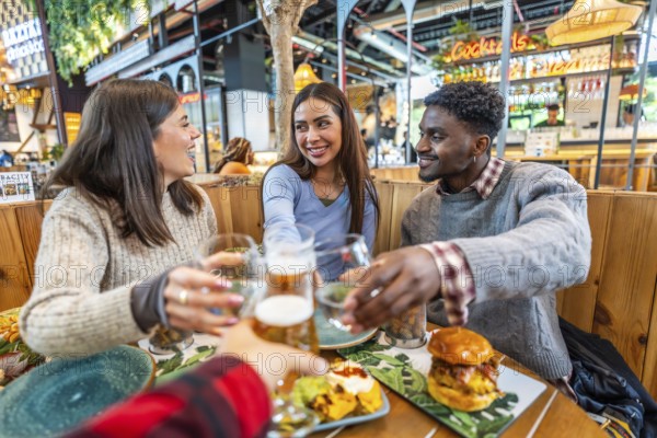 Group of cheerful multi ethnic friends toasting with beer and cocktails, enjoying meal together at