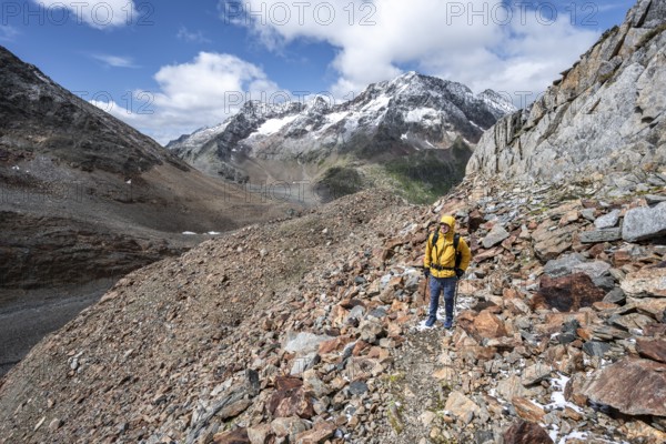Mountaineer on hiking trail in steep rocky mountain landscape with fresh snow in summer, behind