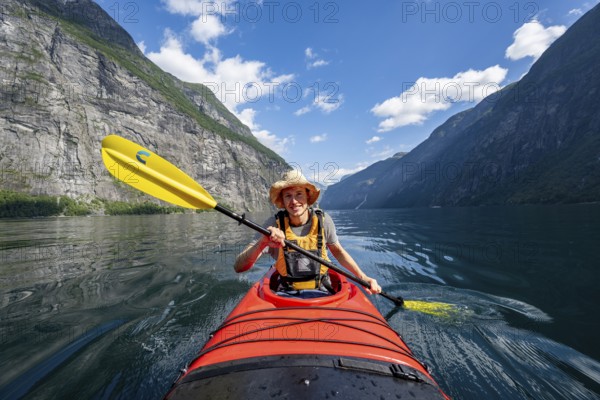 Kayak trip on the Geirangerfjord, young man paddling in red kayak, atmospheric fjord landscape,