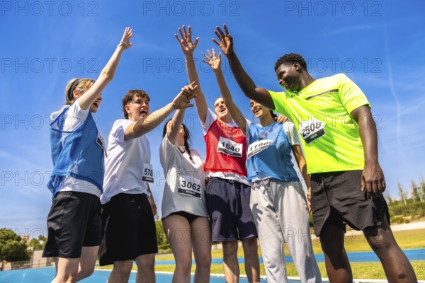 Group of young athletes celebrating their victory on a running track, raising hands together in a