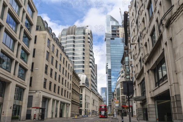 Red double decker bus driving on empty street surrounded by modern and historic buildings in city