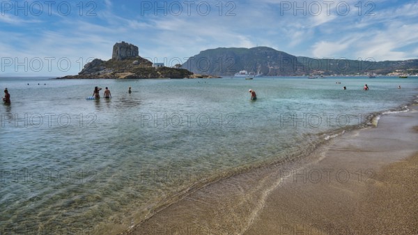 Clear sea with people bathing, surrounded by an island and mountains under a cloudy sky, Agios
