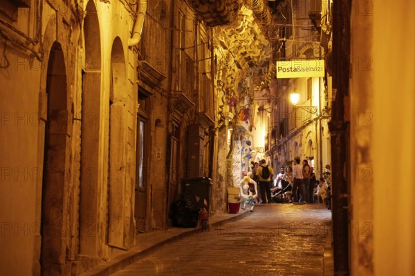 Atmospheric nocturnal alley with warm light and people in front of historic buildings under a