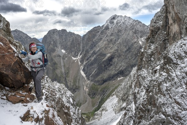 Female mountaineer on a rope-secured climb in a steep rocky mountain landscape with fresh snow in