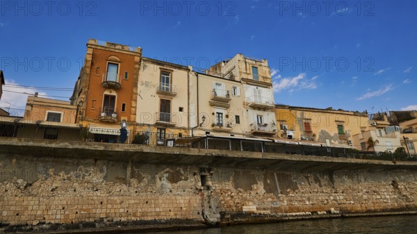 Houses with different facades on a stone coastal wall under a sunny sky, boat trip around the