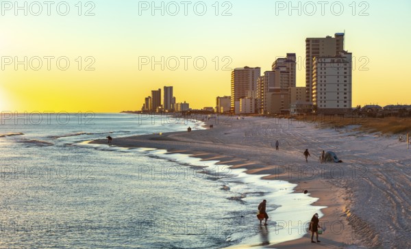 People walking and playing on the beach as the sun sets over the Gulf of Mexico at Gulf Shores,