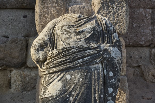 Close-up of a headless stone statue in a landscape of ruins, torso of a statue of a god, Asklipion,