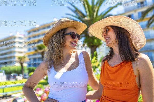 Two happy women wearing sunglasses and straw hats are enjoying their summer vacation in juan les