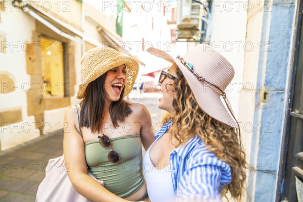Two happy female tourists wearing summer hats are taking a selfie with a smartphone while walking