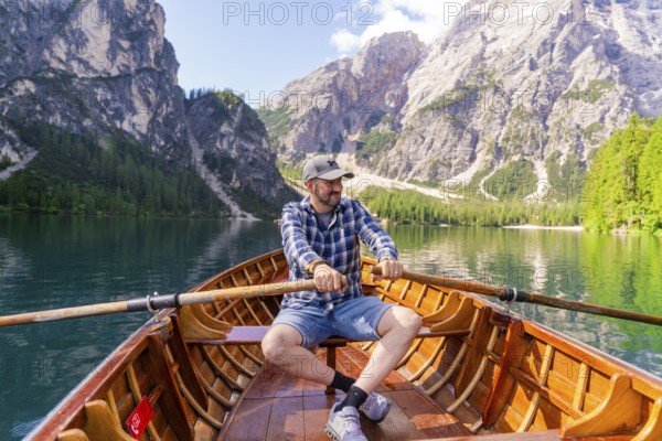 Man rowing on a mountain lake, surrounded by pine trees and steep mountain slopes, Lake Braies,