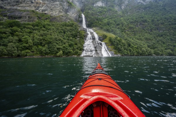 Kayak trip on the Geirangerfjord at the Freier waterfall, tip of a red kayak in the fjord,