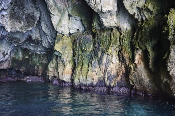Colourful and overgrown rock walls of a grotto directly by the sea, boat trip around the island of