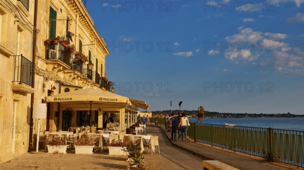 Cosy restaurant on a promenade with sea view. People walking in sunny weather, Ortigia Island,