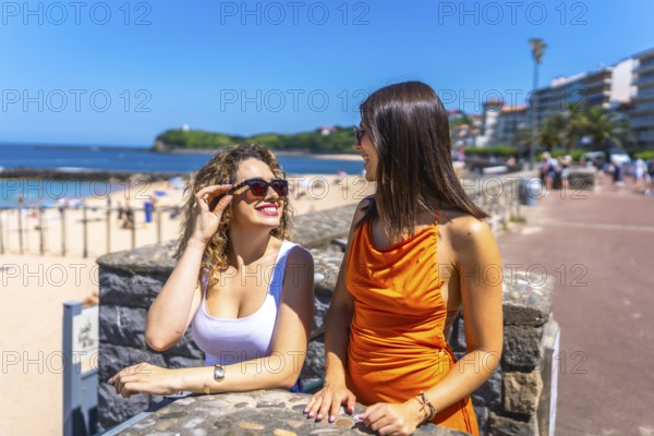 Two cheerful women wearing sunglasses and summer outfits are enjoying their vacation, talking and