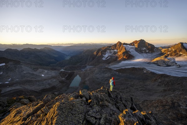 Mountaineer in front of picturesque high mountain landscape at sunrise with alpenglow, blue glacial